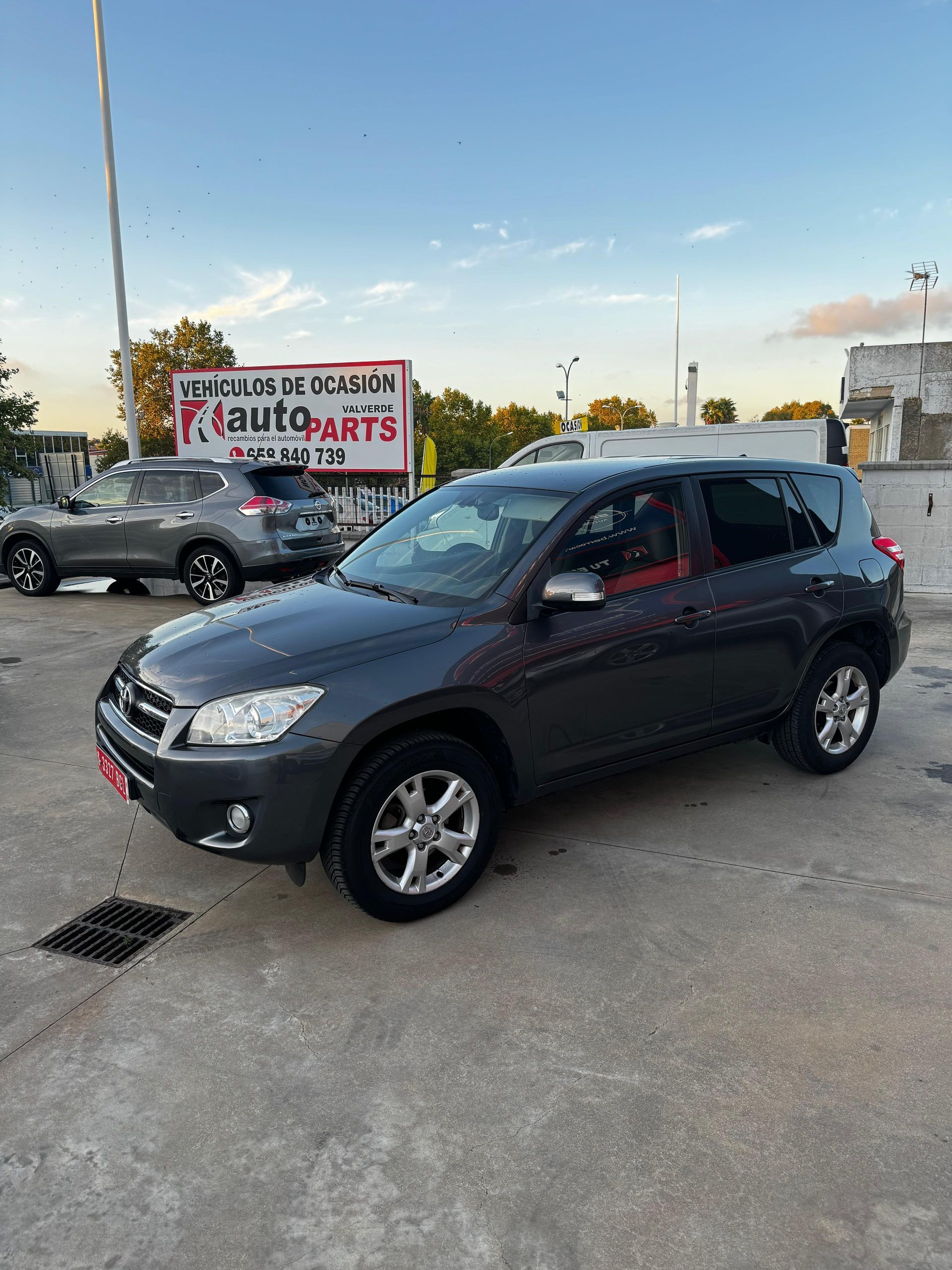 Un Toyota RAV4 gris oscuro estacionado en un lote de concreto frente a un edificio con un letrero que dice 