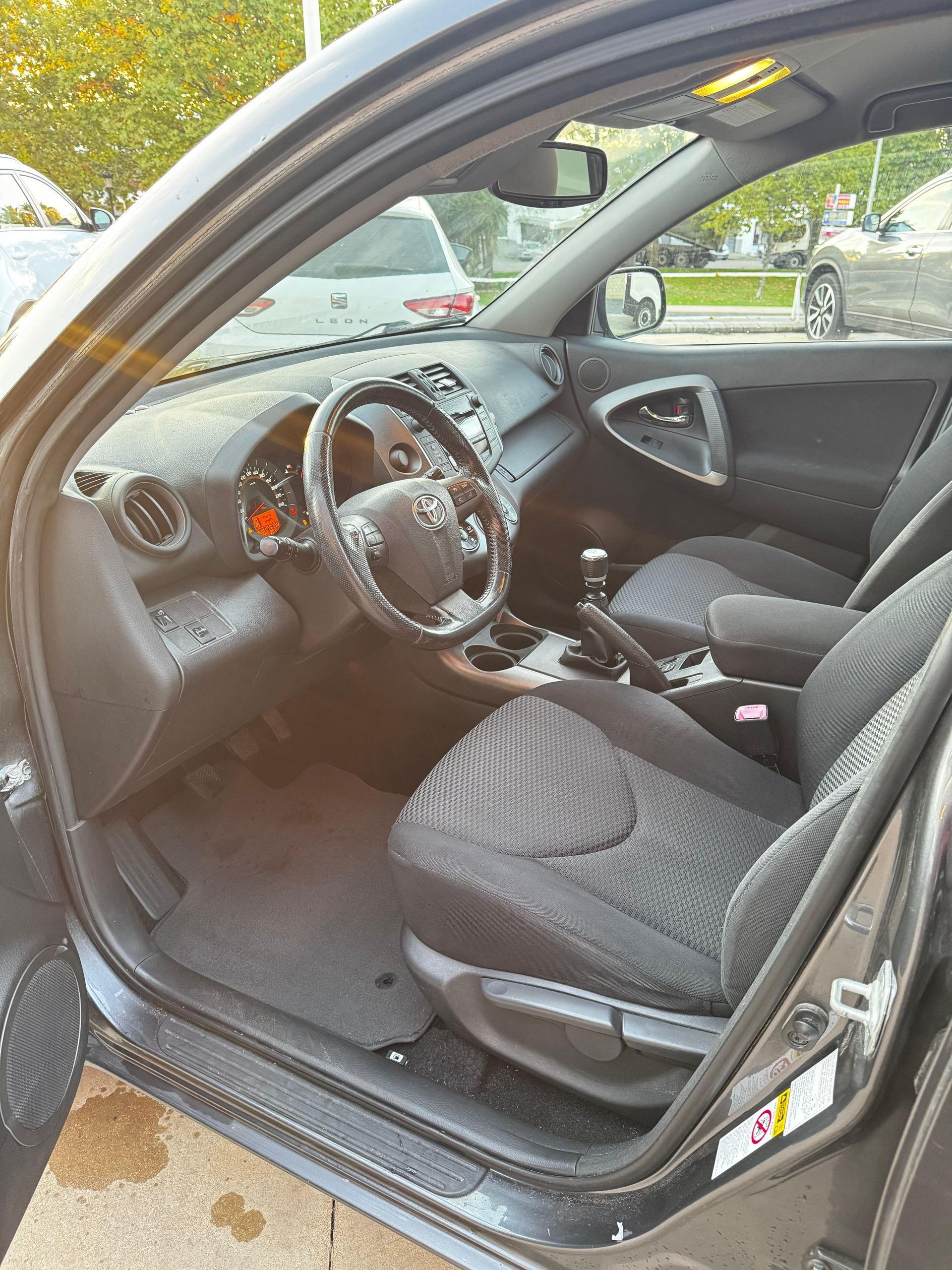 Vista interior de un Toyota RAV4 negro con asientos de tela negra. La puerta del conductor está abierta