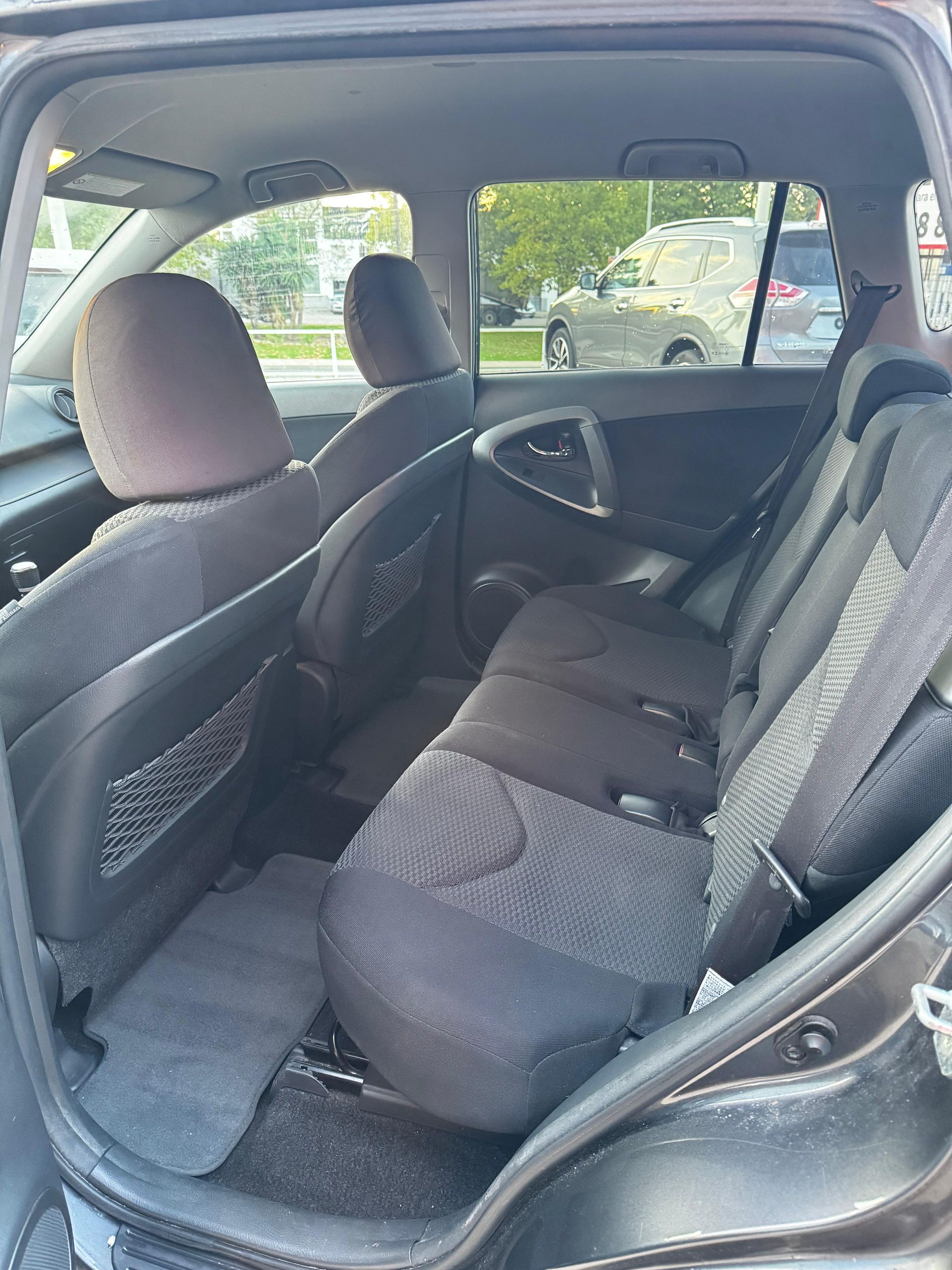 Vista interior de los asientos traseros de un coche, donde se aprecian los asientos de tela negra y la alfombrilla