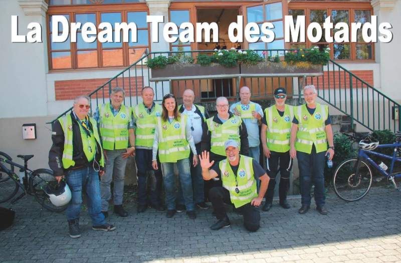 Un groupe de personnes debout devant un bâtiment sur lequel est écrit la dream team des motards
