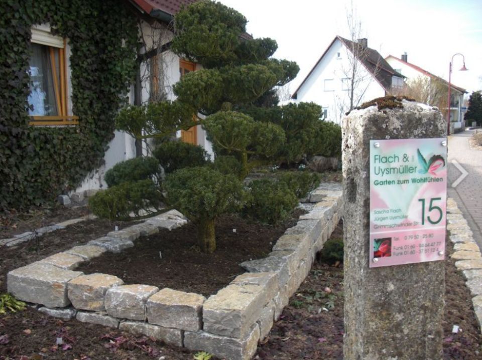 Bepflanzter Bereich mit Steinumrandung und Schild von Flach & Uysmüller GbR
