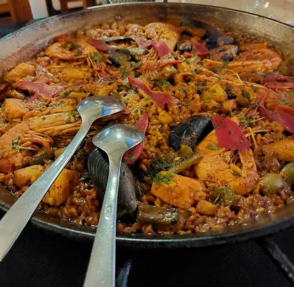 Una cacerola con comida y dos cucharas dentro sobre una mesa.