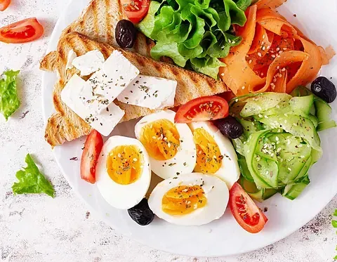 Un plato de comida con huevos duros, tomates, pepinos, aceitunas y tostadas.