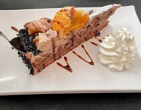 Una rebanada de pastel de chocolate con crema batida en un plato blanco con un tenedor.