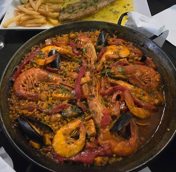 Una sartén llena de camarones, mejillones y arroz junto a un plato de papas fritas.