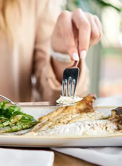 Una mujer está comiendo un plato de comida con un tenedor.
