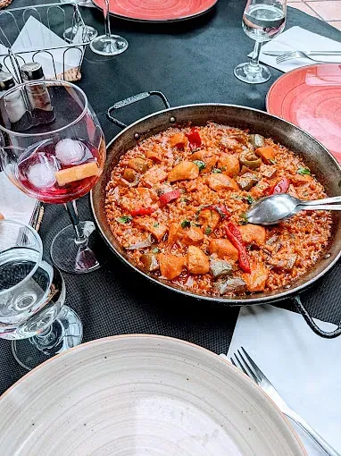 Una cacerola con comida está sobre una mesa al lado de una copa de vino.