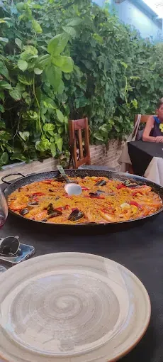 Una gran sartén con paella está sobre una mesa al lado de un plato.