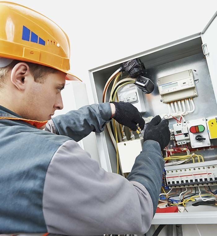 Un hombre que lleva un casco naranja está trabajando en una caja eléctrica.