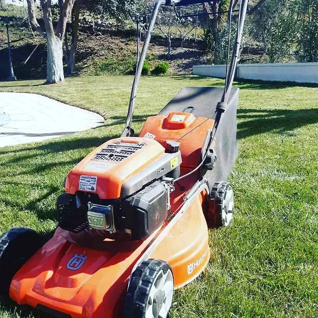 Una cortadora de césped Husqvarna naranja está estacionada en el césped.