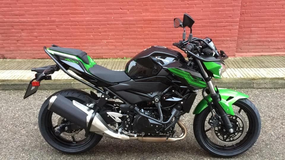 Una motocicleta negra y verde está estacionada frente a una pared de ladrillos rojos.