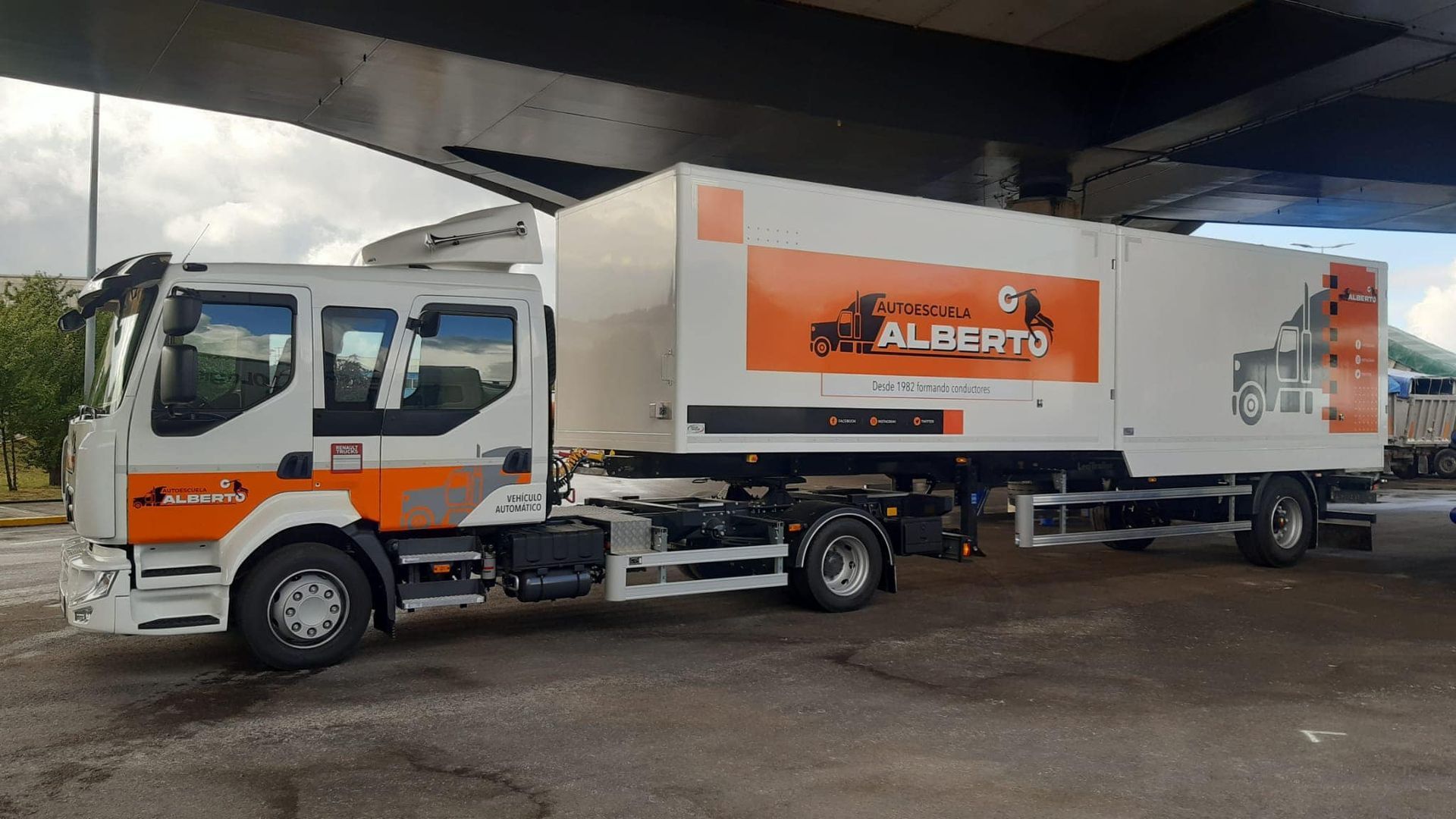 Un camión blanco y naranja está estacionado debajo de un puente.