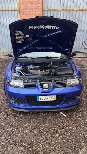 Seat León azul con el capó abierto, estacionado frente a un edificio. El coche tiene características personalizadas y matrícula.