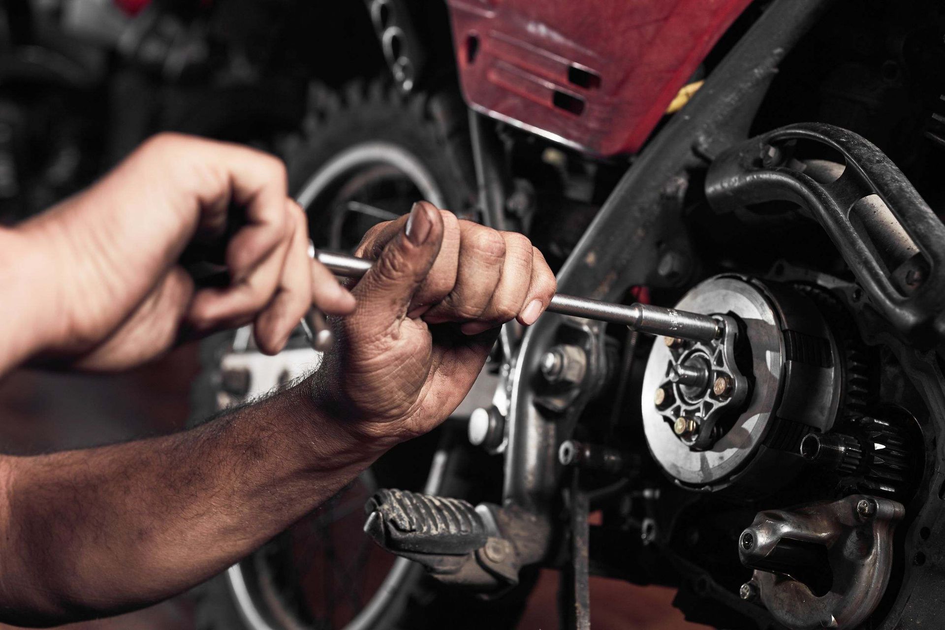 Manos de una persona trabajando en el motor de una motocicleta con una llave inglesa. Un primer plano muestra las manos sucias en un taller.
