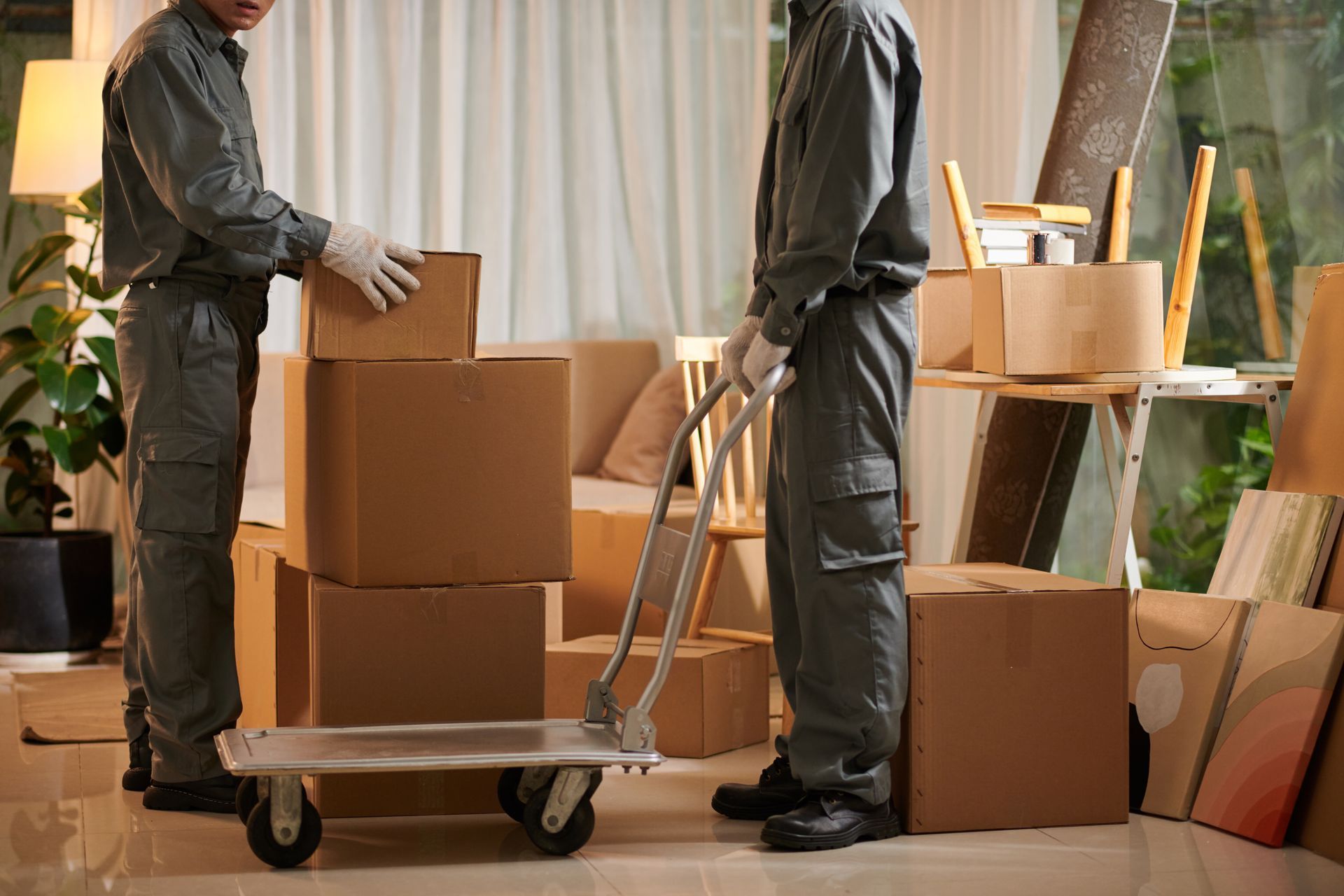 Deux silhouettes d'hommes en combinaison grise chargeant des cartons sur un diable