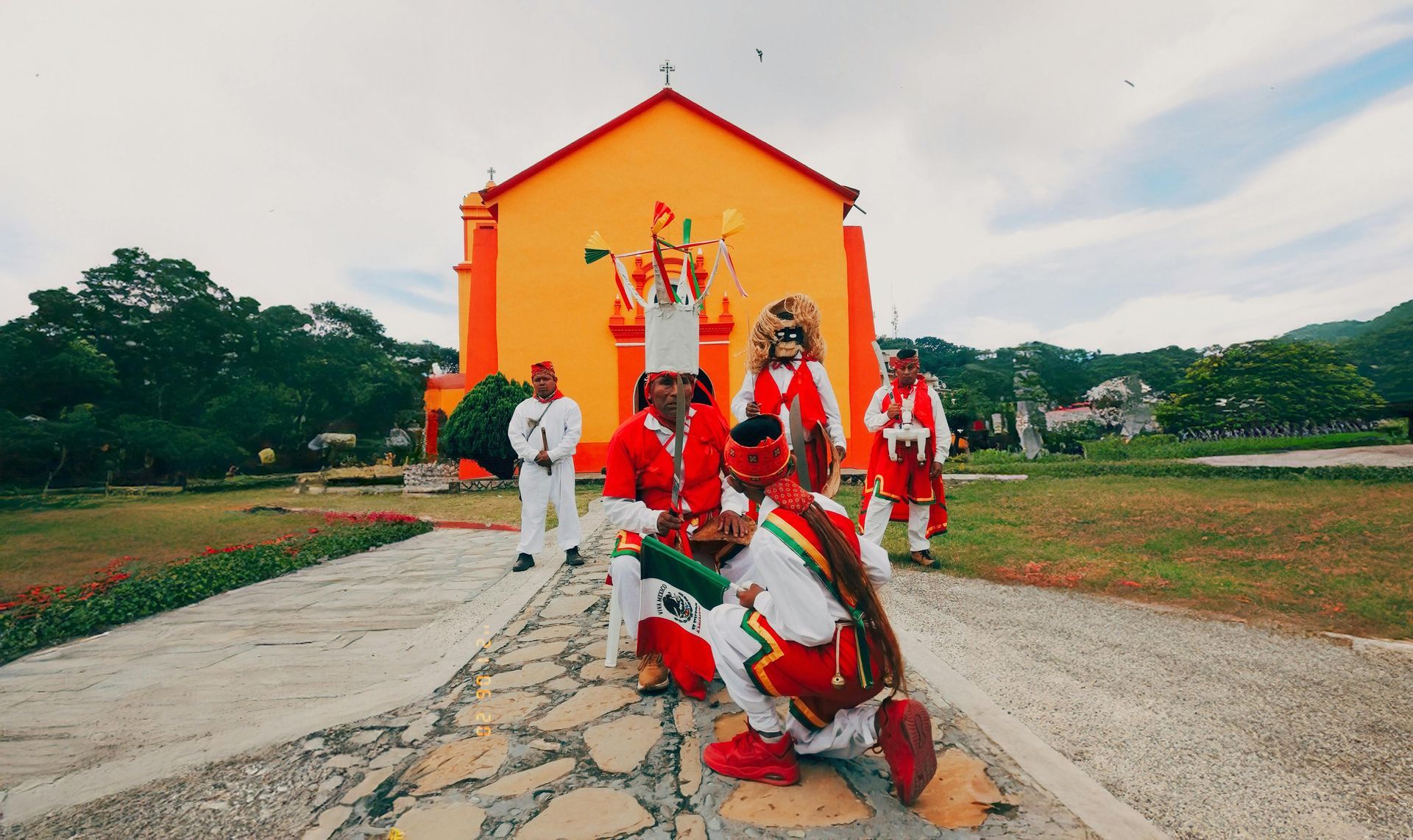 Personas vestidas con trajes rojos y blancos posando frente a un edificio naranja en un sendero de piedra.