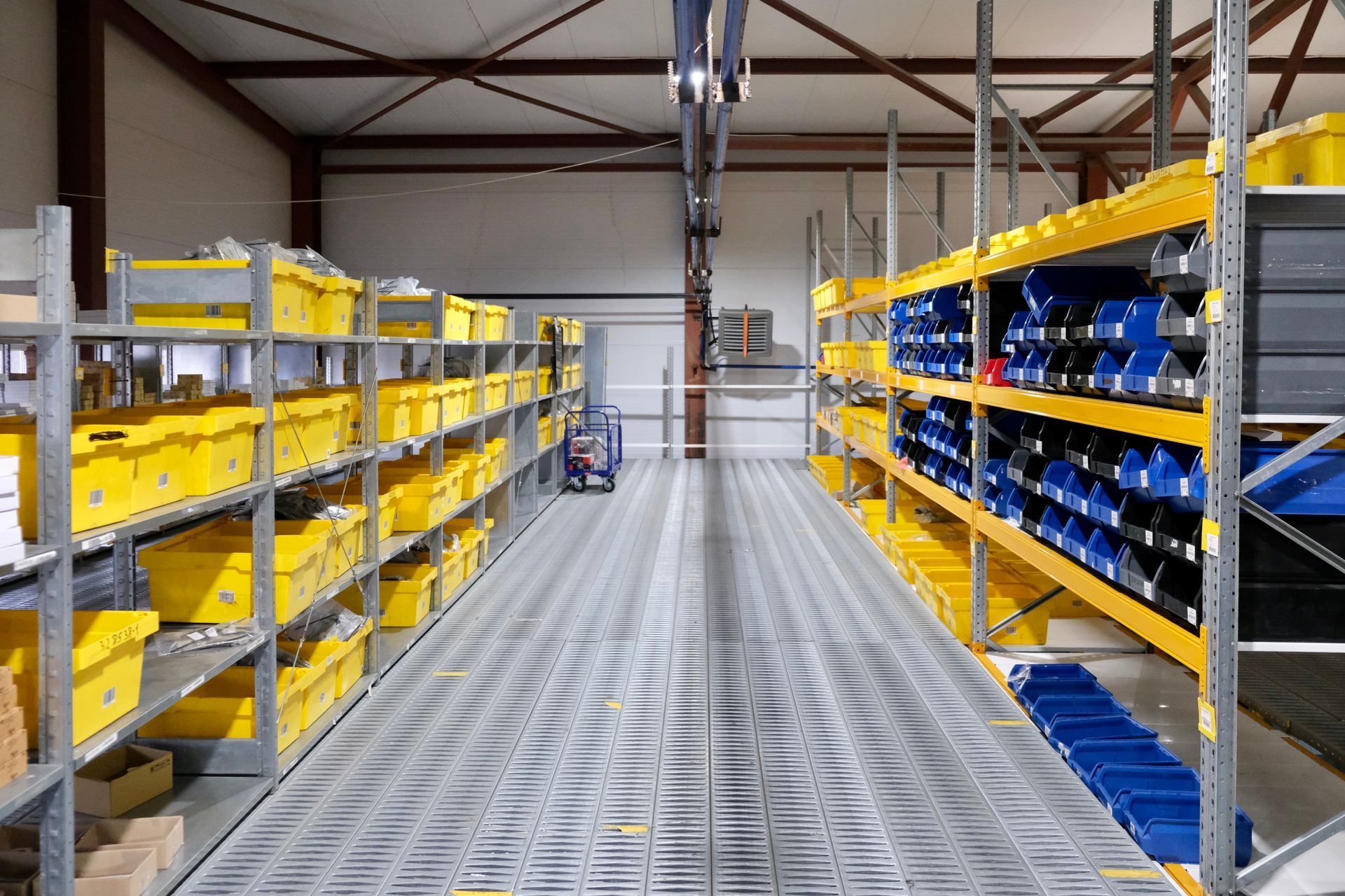 Intérieur d'un entrepôt avec des rangées d'étagères remplies de bacs jaunes et bleus.