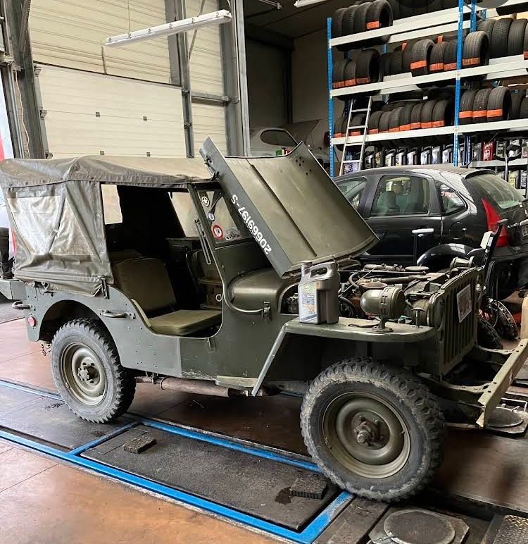 Jeep militaire verte, capot ouvert, dans un garage.