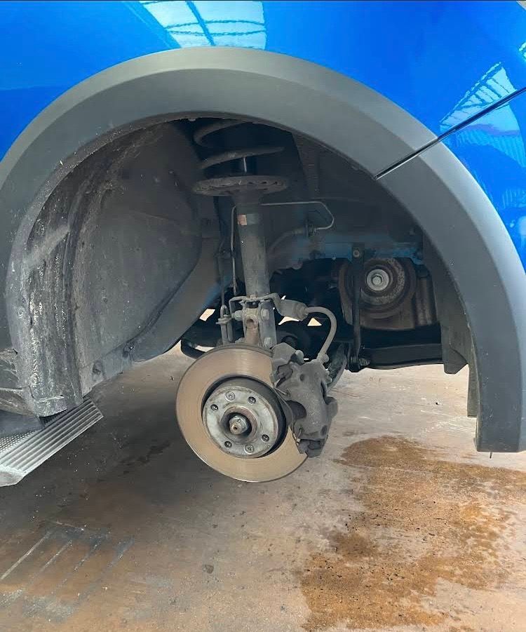 La roue avant d'une voiture bleue a été retirée, révélant le disque de frein, la suspension et l'aile.