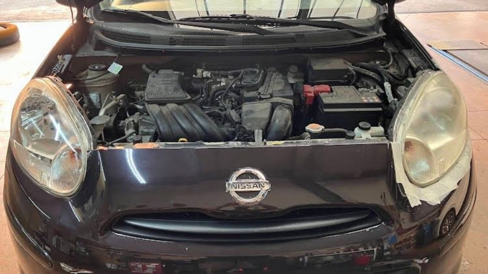 Voiture Nissan noire, capot ouvert, laissant apparaître le compartiment moteur et les optiques en rénovation.