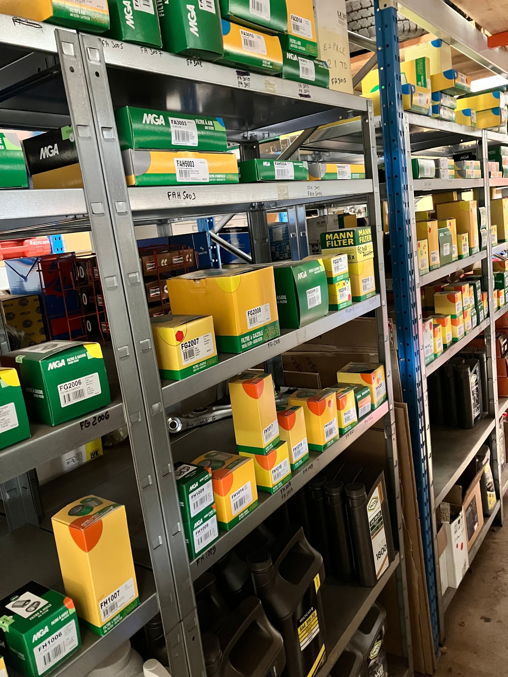 Des étagères remplies de pièces automobiles dans des boîtes et des conteneurs de couleurs variées, dans un magasin de pièces détachées.