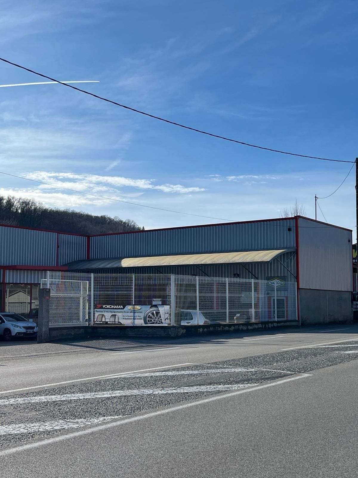 Garage automobile avec bardage métallique gris et rouge et une clôture blanche en bordure de rue.