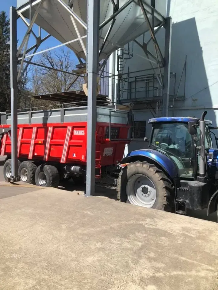 Tracteur bleu garé à côté d'une remorque rouge sous une structure métallique à l'extérieur