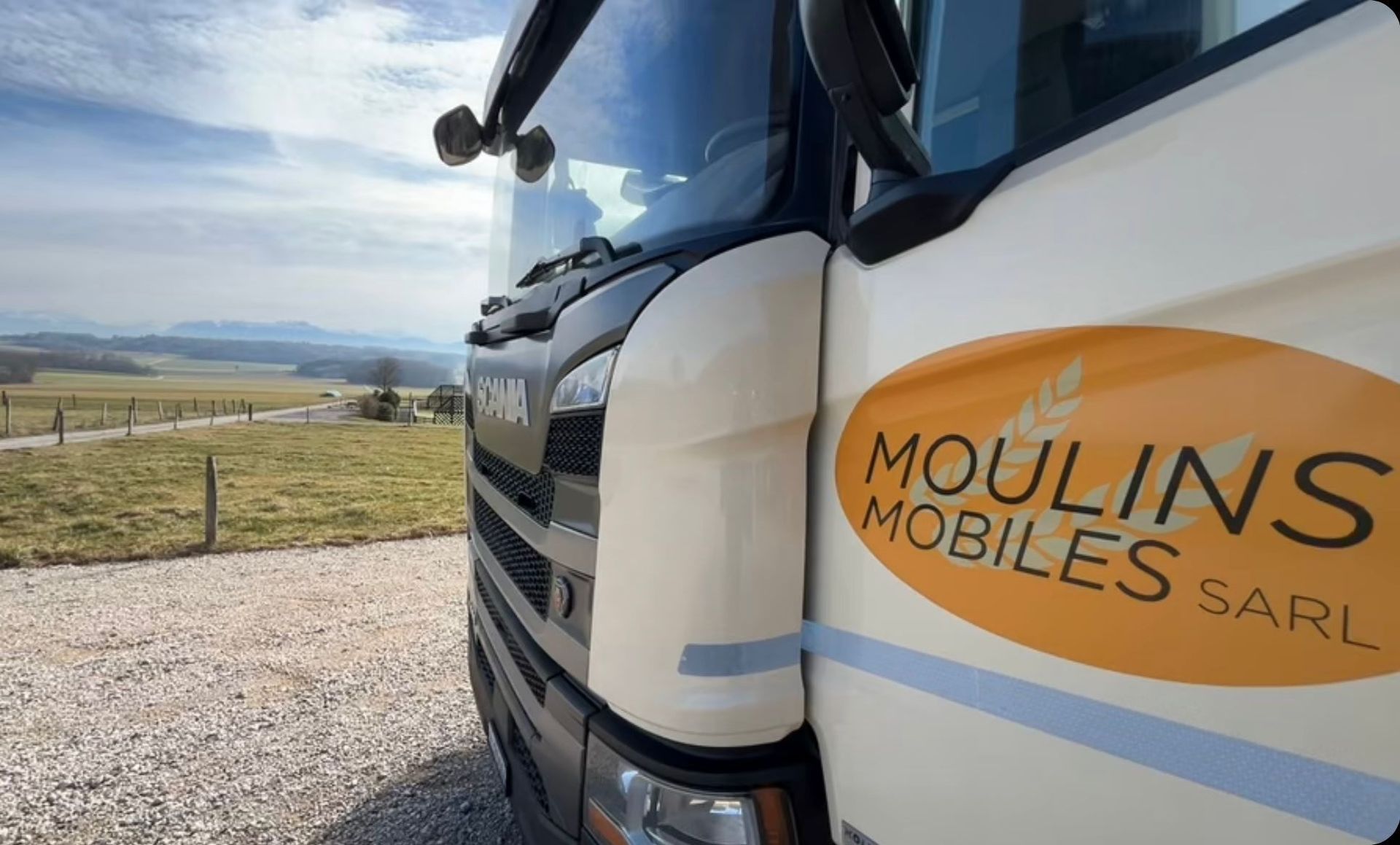 Gros plan sur un camion de livraison blanc portant le logo « Moulins Mobiles », stationné dans un paysage rural.