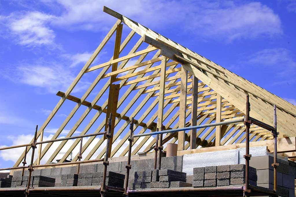 Charpente d'une maison en construction avec fermes de toit en bois apparentes sur fond de ciel bleu