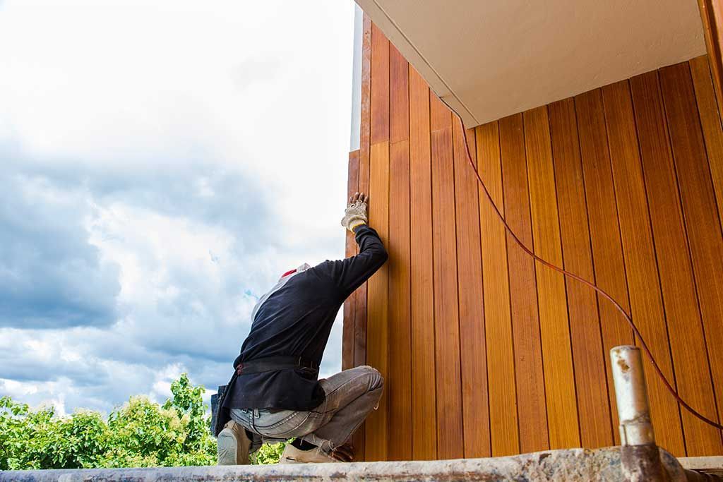 Installation par un professionnel de bardage en bois à l'extérieur sous un ciel nuageux