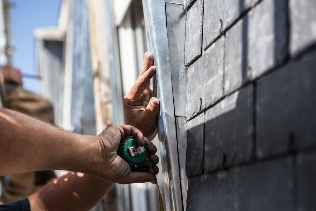 Des mains posent des carreaux muraux foncés à l'aide d'un outil de mesure sur un mur extérieur en ardoises
