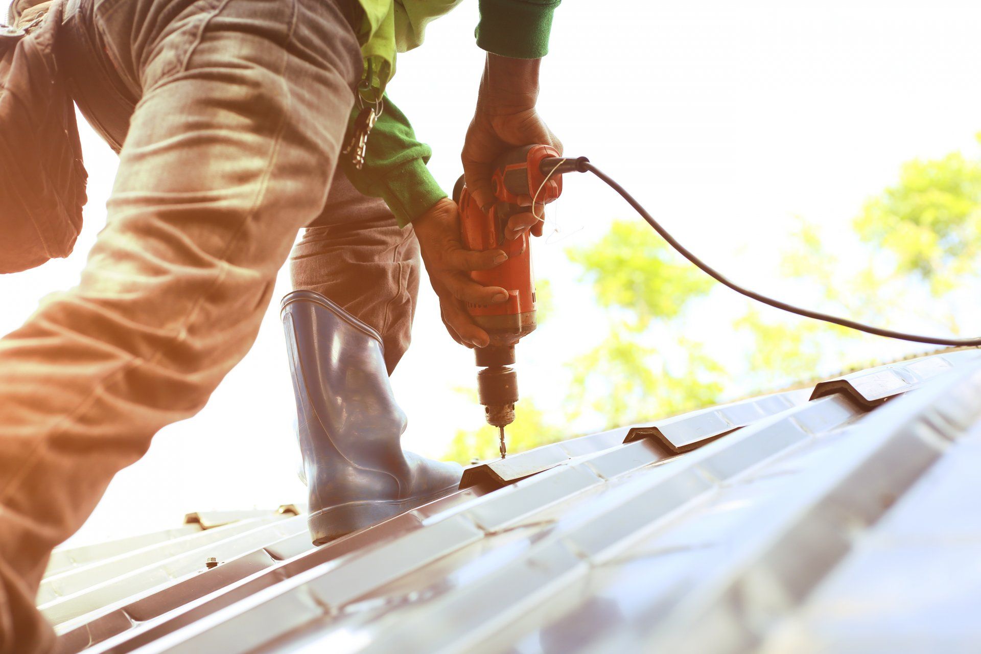 Ouvrier utilisant une perceuse électrique sur un toit métallique en plein soleil