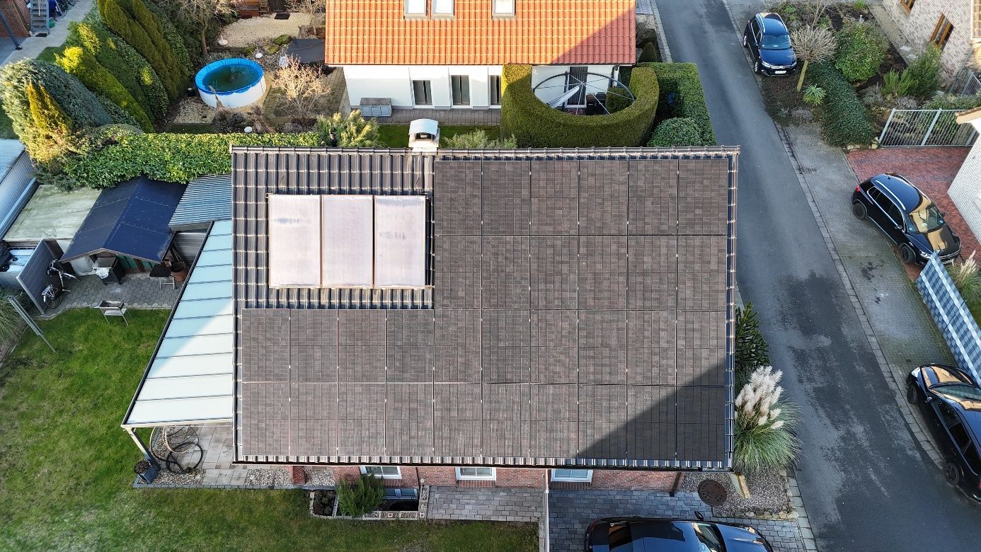 Luftaufnahme eines Hauses mit Solarpaneelen auf dem Dach. Autos parken auf einer Straße.