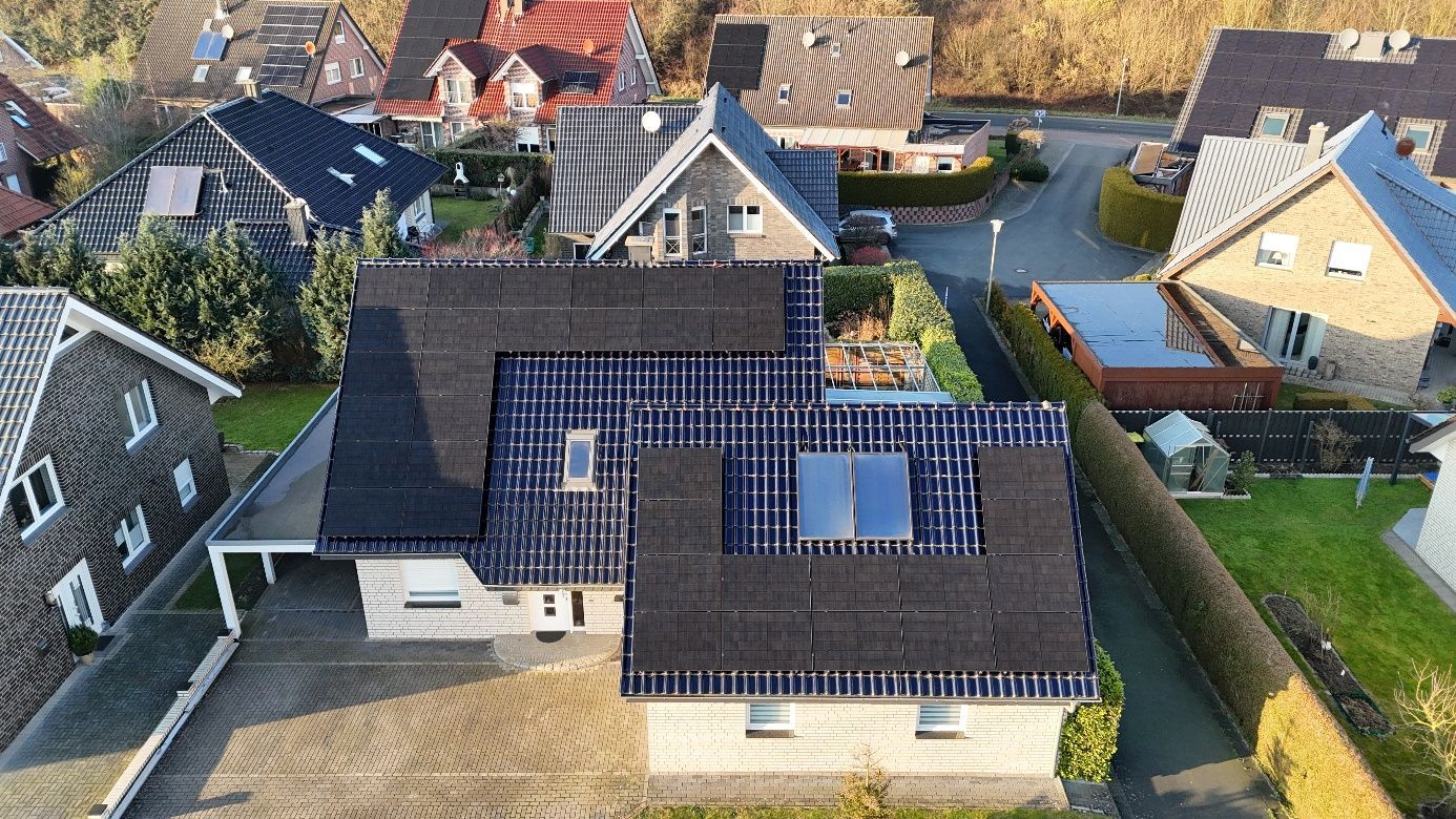 Draufsicht auf ein Haus mit Solarpaneelen auf schwarzem Dach in einem Wohngebiet.