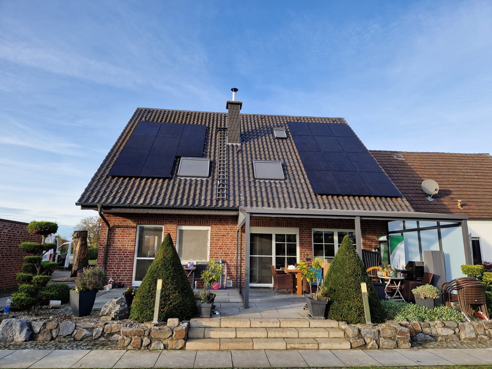 Haus mit Solarpaneelen auf dem Dach, Treppe zu einer Terrasse und einem gepflegten Garten.