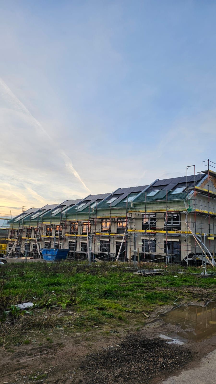 Eine Reihe im Bau befindlicher Reihenhäuser; Gerüste, Gründächer, Solarpaneele, bedeckter Himmel.