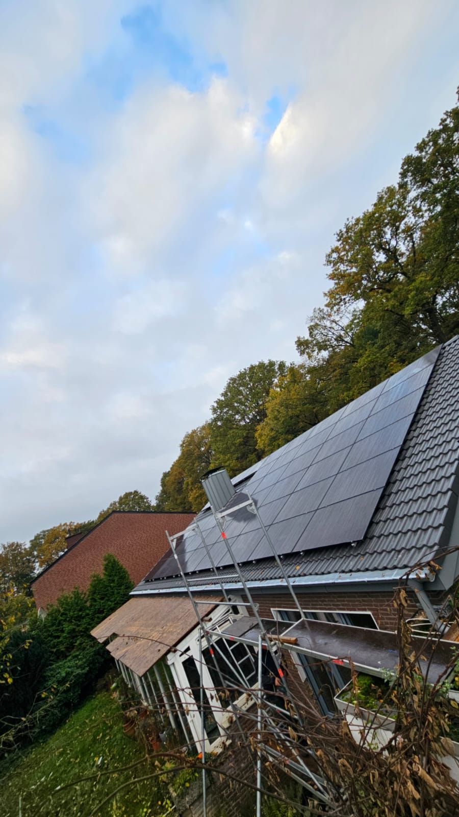 Solarpaneele auf einem Ziegeldach eines Hauses, vor einem bewölkten Himmel und Bäumen.