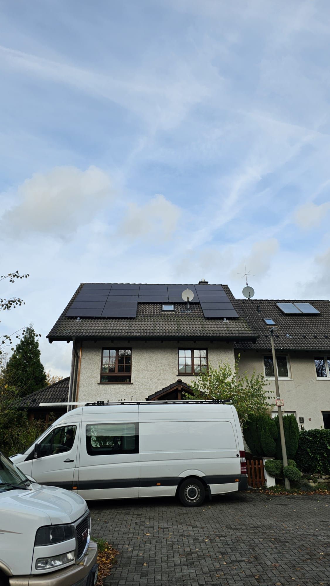 Solarpaneele auf dem Dach, weißer Lieferwagen davor geparkt, bedeckter Himmel.