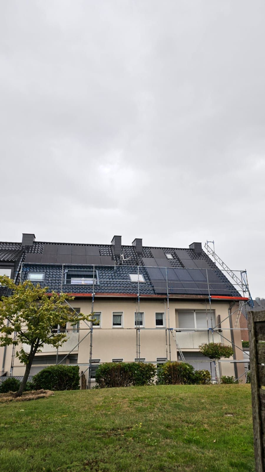 Dach eines Wohngebäudes mit Solarpaneelen und Gerüst unter bewölktem Himmel.
