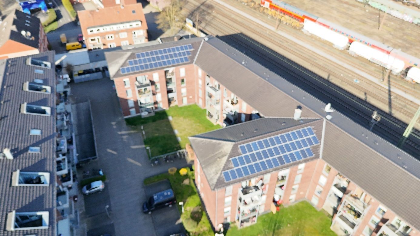 Luftaufnahme eines Backstein-Wohnhauses mit Solarpaneelen auf dem Dach neben einer Eisenbahnlinie und einem Zug.