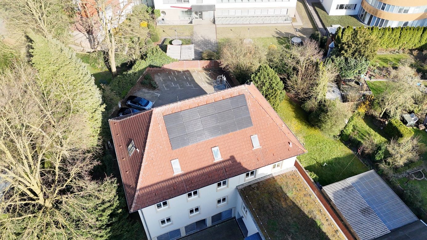 Luftaufnahme eines Hauses mit Solarpaneelen auf einem roten Ziegeldach, umgeben von Bäumen und einem grünen Rasen.