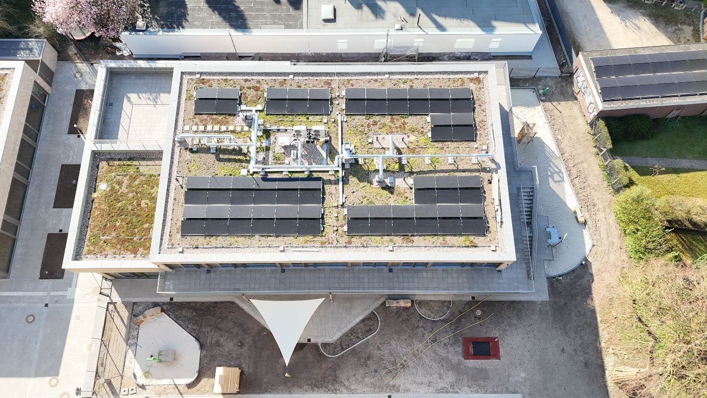 Draufsicht auf ein Flachdach mit Solarpaneelen und Begrünung, neben einem Gebäude und weiterer Begrünung.