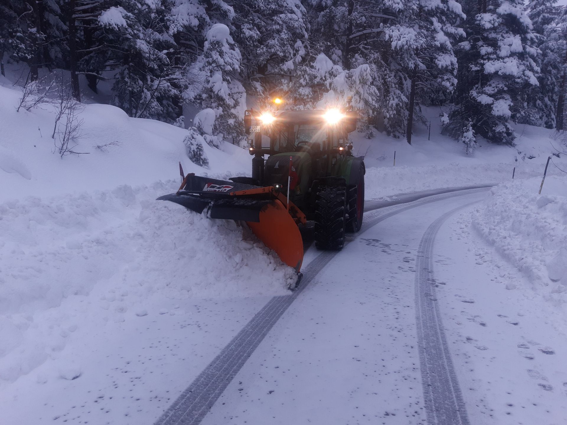 Schneepflug bei der Räumung einer verschneiten Straße im Wald während der Dämmerung.