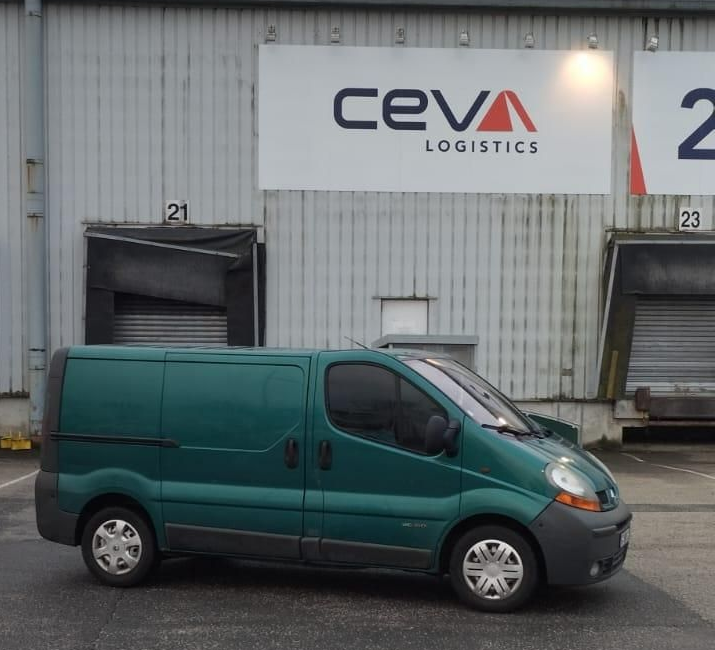Camionnette de livraison verte stationnée devant un entrepôt de CEVA Logistics.