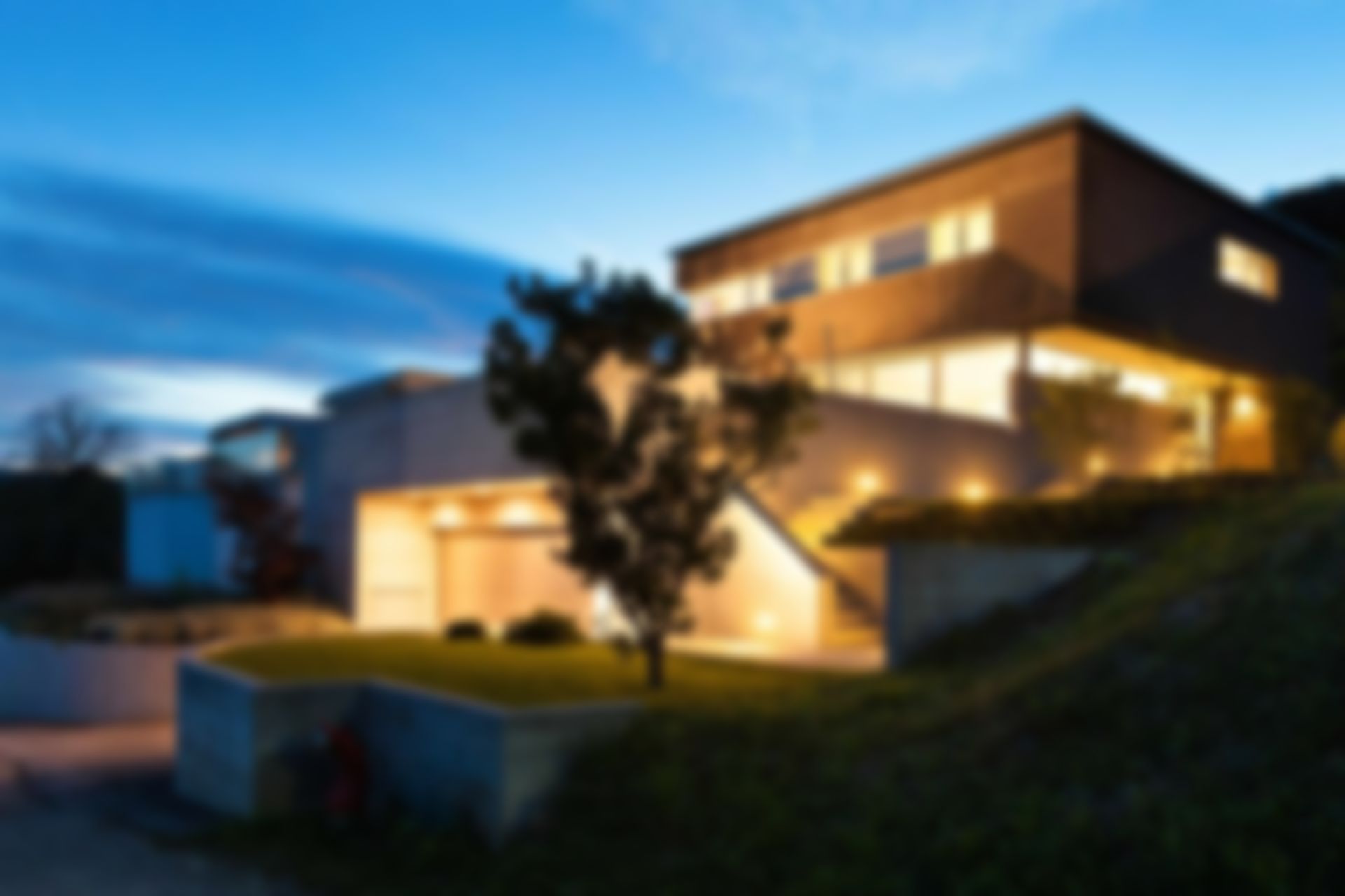 Una casa grande está iluminada por la noche con un árbol delante de ella.