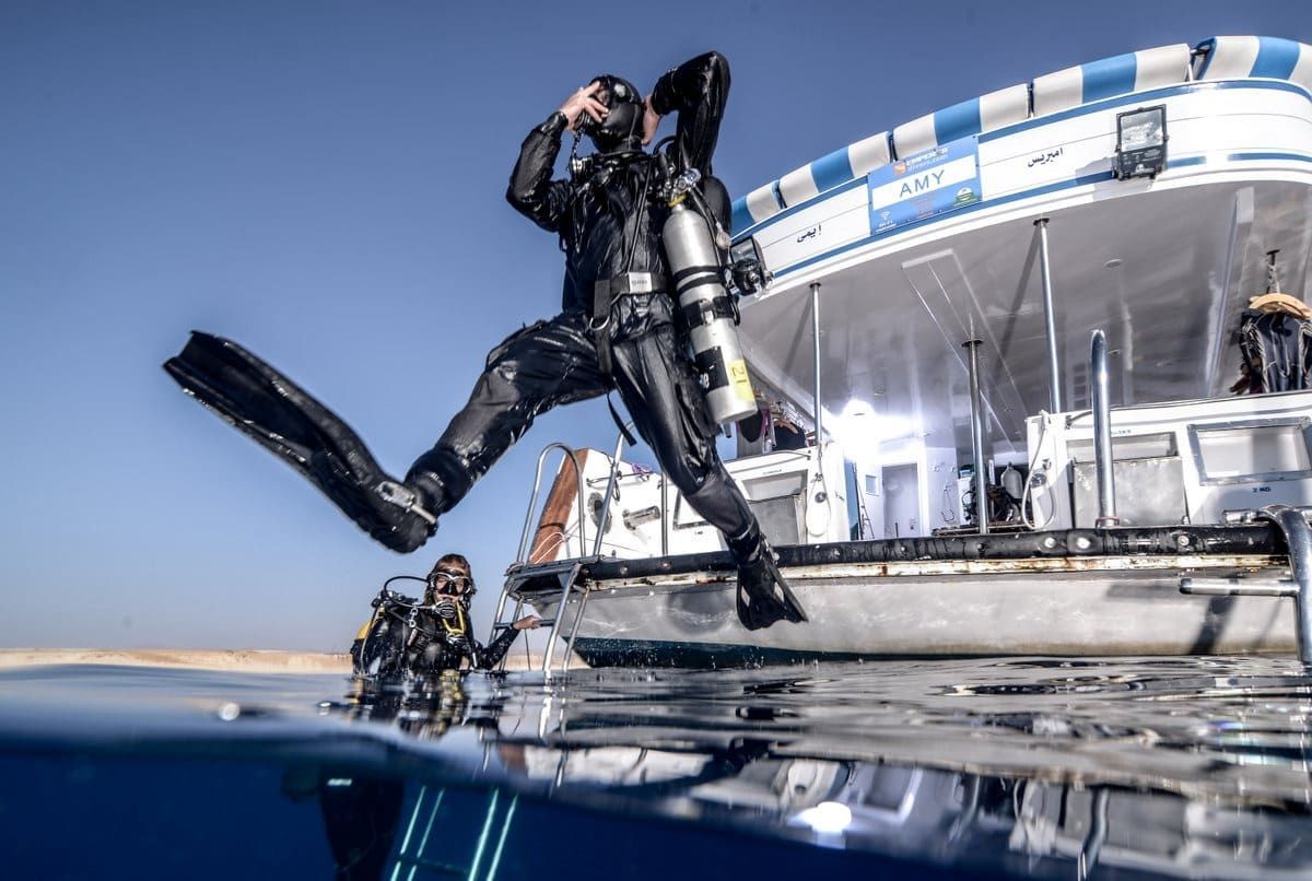 Un buceador salta desde un barco a las aguas cristalinas junto a un yate atracado.