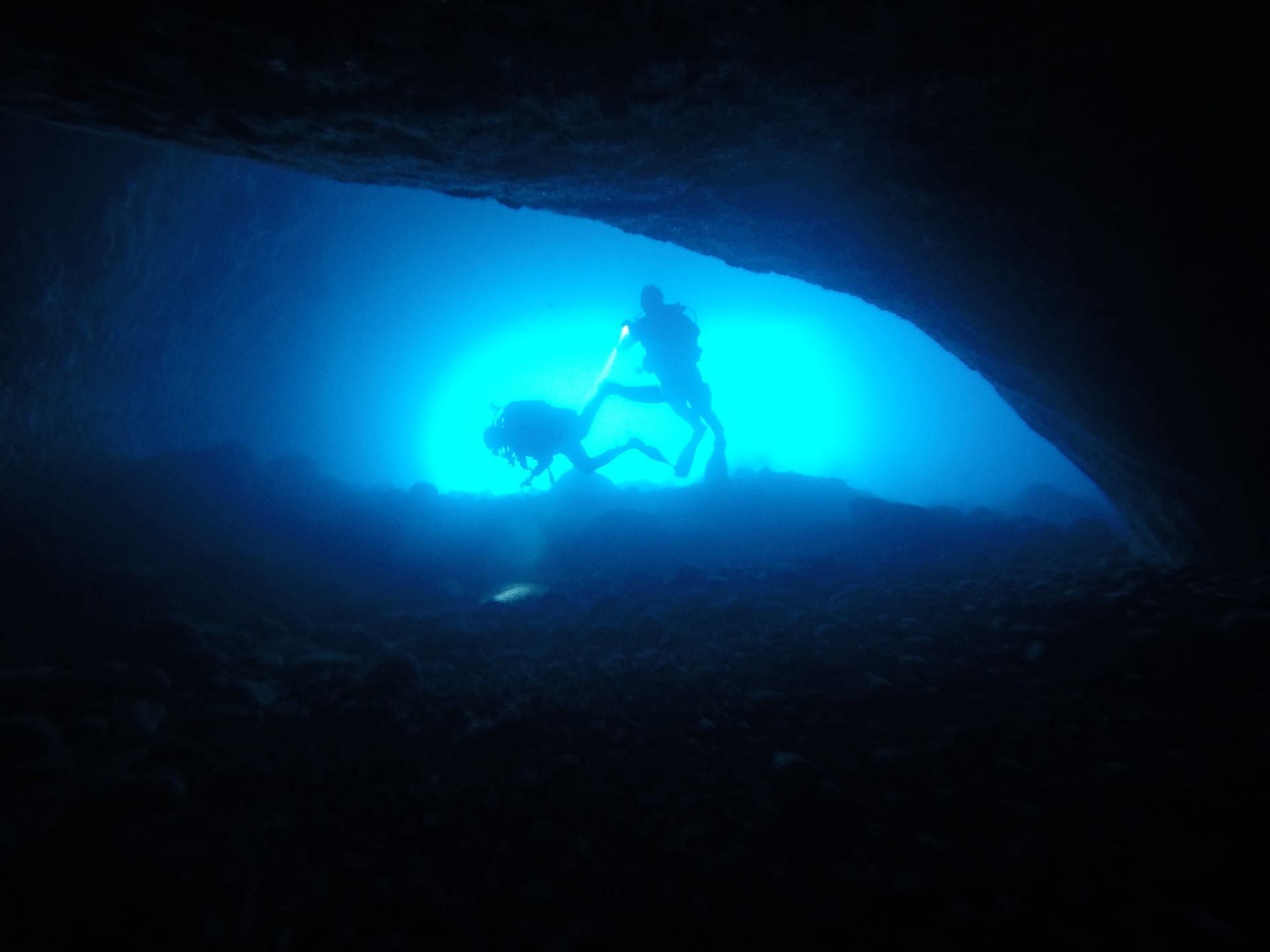 Silueta de un buceador en una cueva submarina de color azul brillante.