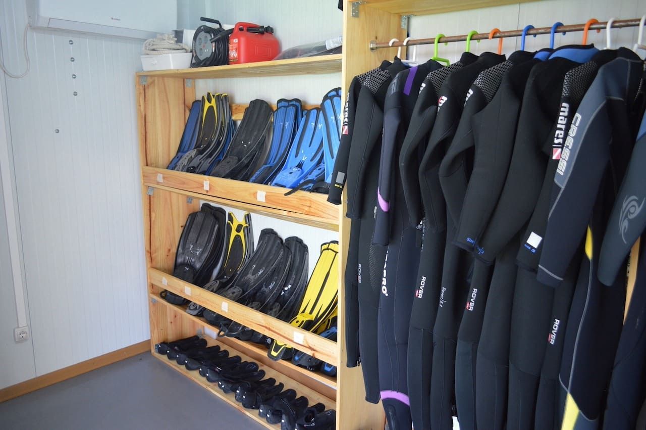 Una hilera de trajes de neopreno negros y chaquetas azules colgadas en un estante de equipo.