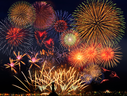 Fuegos artificiales de colores estallan en el oscuro cielo nocturno sobre espectadores cuyas siluetas se recortan contra el cielo.