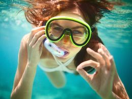 Persona sumergida con una máscara de snorkel verde, nadando en aguas cristalinas de color azul.
